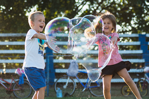Happy children are playing with giant soap bubbles outdoors, joyful childhood concept.