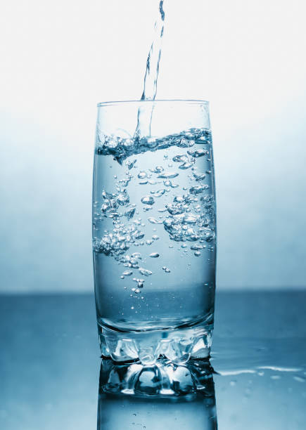istock Drinking water poured into a glass isolated over blue abstract background. Space for text 1257819966