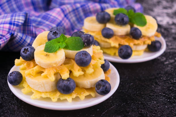 Two portions of waffles with berries and banana on a white plate. Close-up. Delicious breakfast.