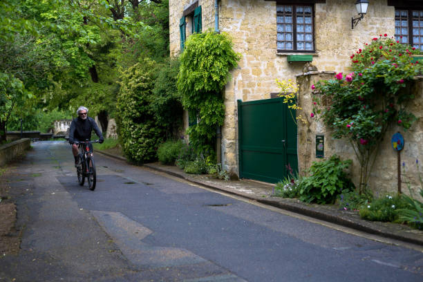 Riding a bike in France Auvers Sur Oise, France.  May 10, 2019.  A man riding a bicycle  pedals down a french country lane.  Stone building in the background showing architecture of the area. auvers sur oise photos stock pictures, royalty-free photos & images
