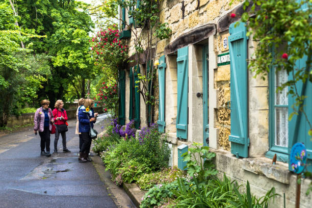 Admiring the architecture in France. Auvers Sur Oise, France.  May 10, 2019. A group of woman admire the flowers and windows of the architecture in a small town in France.  The building is adorned with blue shutters and flowering plants. auvers sur oise photos stock pictures, royalty-free photos & images