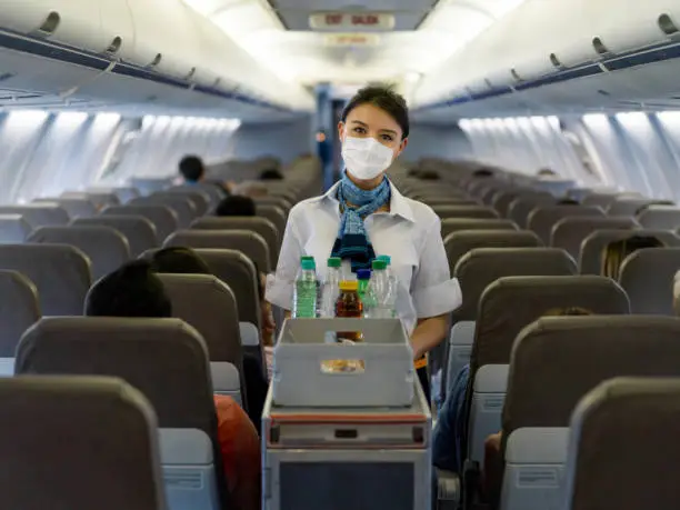 Portrait of a flight attendant serving food and drinks in an airplane wearing a facemask during the COVID-19 pandemic