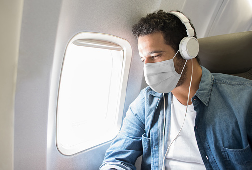 Portrait of a Latin American man listening to music while flying on an airplane wearing a facemask to avoid the coronavirus