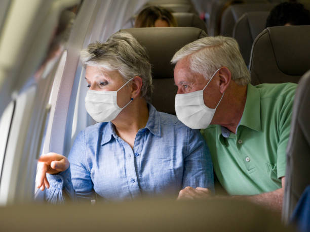 Senior couple traveling by plane wearing facemasks Latin American senior couple traveling by plane wearing facemasks and looking through the window - travel during the COVID-19 pandemic window seat vehicle stock pictures, royalty-free photos & images