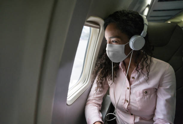 frau hört musik, während sie in einem flugzeug mit einer gesichtsmaske fliegt - fensterplatz fahrzeugsitz stock-fotos und bilder