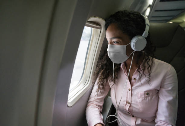 Woman listening to music while flying on an airplane wearing a facemask Portrait of an African American woman listening to music while flying on an airplane wearing a facemask during the COVID-19 pandemic n95 face mask photos stock pictures, royalty-free photos & images