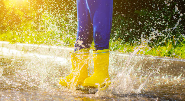 My rubber-booted feet are Bouncing in a puddle. Article about rubber boots. Children's summer shoes. Puddles after rain. Bad weather. A child jumps in a puddle. Happy childhood. A happy boy in rubber boots jumps in puddles.