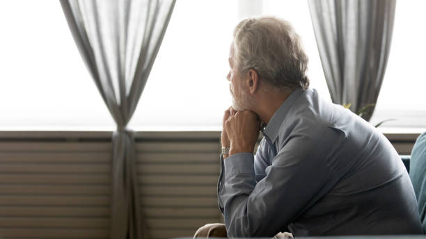 istock Rear view sad older man looking in window, sitting alone 1257831229