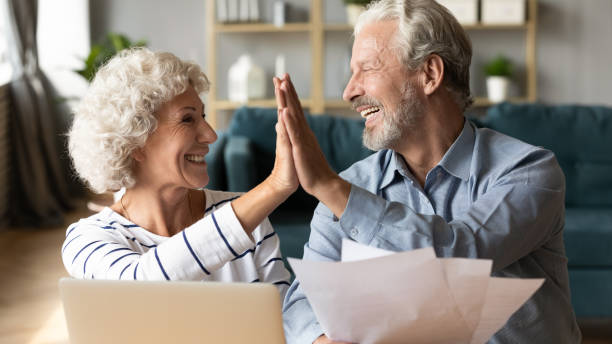 pareja mayor emocionada dando cinco altos, celebrando buenas noticias - pension retirement planning savings fotografías e imágenes de stock