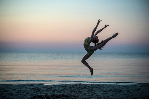 A female flexible dancer in swimming suit jumping during sunset at the beach