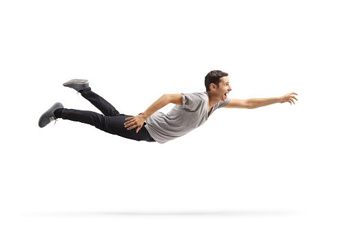 Full length profile shot of a casual young man flying and reaching for something isolated on white background