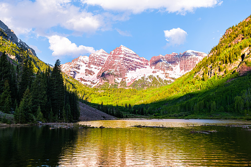Maroon Bells lake peak at sunrise panoramic view in Aspen, Colorado with rocky mountains snow in July 2019 summer and bright sunny light reflection on water