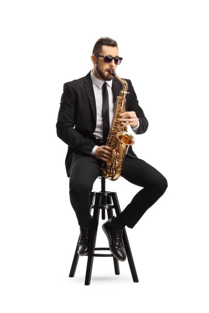 istock Handsome man in a black suit playing a saxophone and sitting on a chair 1257835749