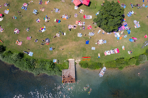 Aerial view of a beach at the lake with a large group of people swimming and sunbathing.