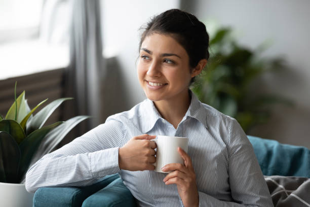 istock Smiling young indian woman relaxing on comfortable sofa, drinking coffee. 1257836845