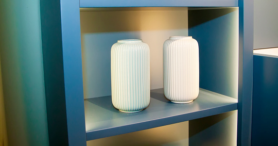 two white ceramic vases on a blue illuminated shelf