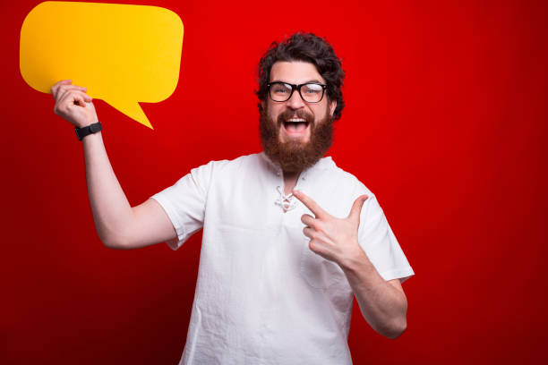 istock Excited bearded hipster is pointing at a yellow bubble speech 1257842541