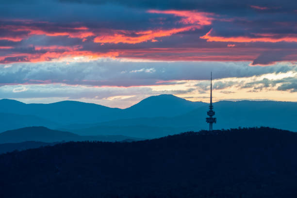 Canberra Telstra Tower during sunset with layers of pink and yellow coloured clouds in the background. Shot from Mount Ainslie during a colourful sunset with mountains at the horizon.