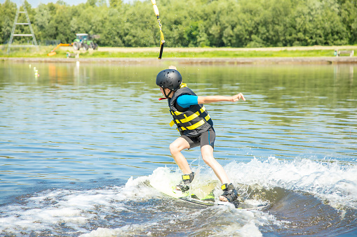 Caucasian boy of 10 years old in a protective suit, active wakeboard training with fun activities in water sports adventure, relaxation and exercise concept. Sports and Hobbies