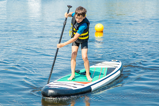 A paddler-boarder. Photo of 10-year-old Boy rowing on standing Board. Healthy lifestyle. Water sports, SUP surfing tour in an adventure camp on active summer sport camp. Healthy active lifestyle