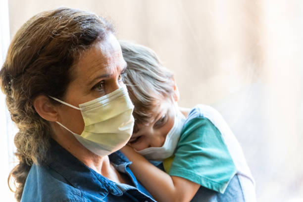 istock Mature woman posing with her son, both with protective masks, very sad looking through window worried about Covid-19 pandemic 1257852069