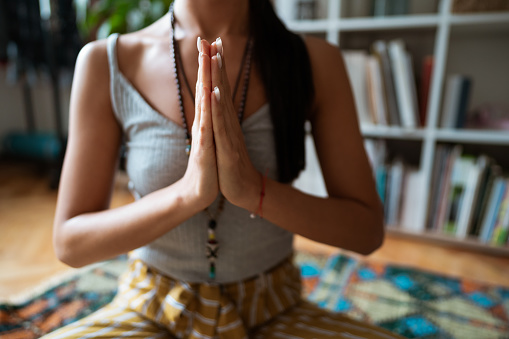 Close-up of a Caucasian woman holding hands in a namaste gesture. She is meditating and praying at home.