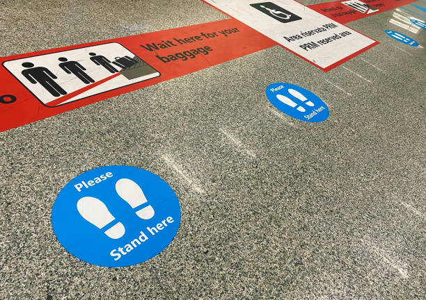 stickers on the floor near the baggage claim belt at the airport that warn of keeping social distance during the health emergency during the coronavirus pandemic - pista de aeroporto imagens e fotografias de stock