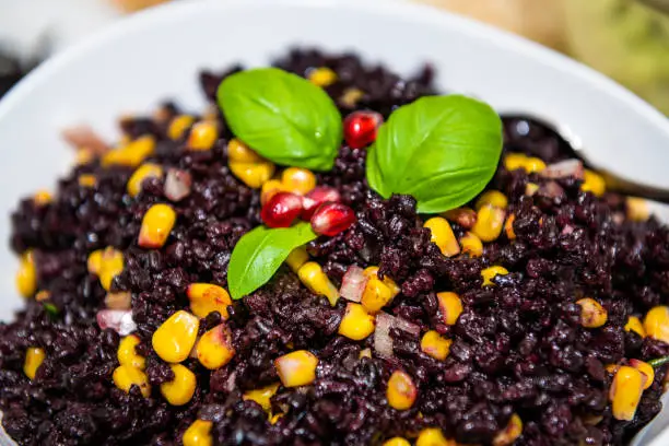 Macro closeup texture of forbidden Chinese black rice dish with corn, vegetables basil leaves decoration on plate bowl isolated