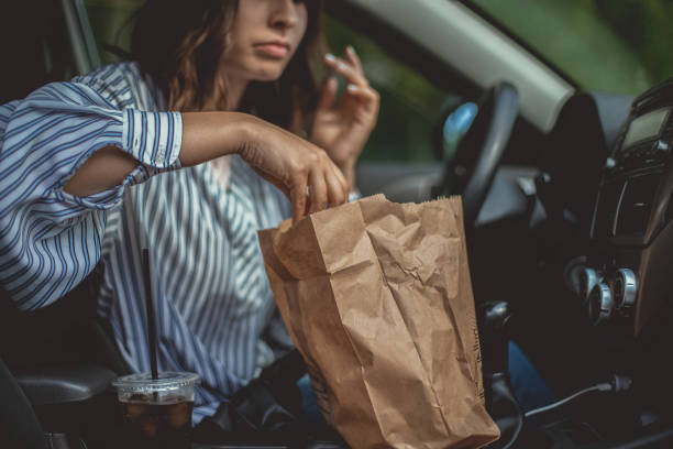 Ready-to-eat! A beautiful young woman is reaching for some french fries in the paper bag and she can't wait to start the brunch in her car. bag lunch stock pictures, royalty-free photos & images