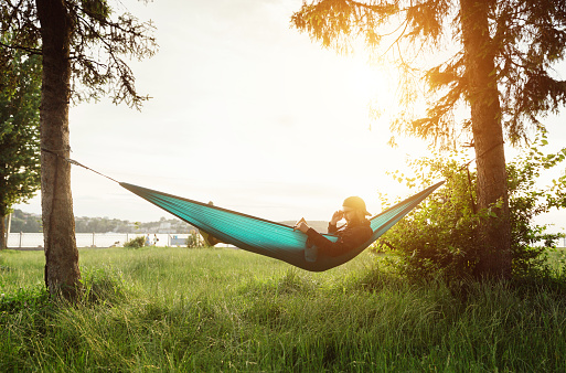 Bearded hipster male reading book in hammock at sunset