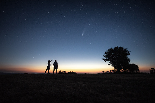 Silhouette of a young couple watching the Neowise comet  under the bright night sky after sunset