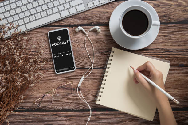 istock podcast audio content concept. podcast application on mobile smartphone screen on wooden table with coffee cup, earphones, glasses, notebook and pencil. broadcast media 1257885172