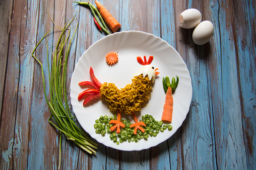 Food art on a background with noodles, vegetables, eggs in the form of rooster on a plate with use of selective focus.