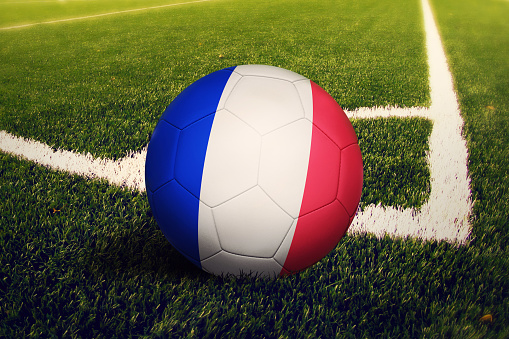 France flag on ball at corner kick position, soccer field background. National football theme on green grass.