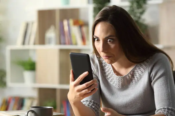 Perplexed woman looking surprised at phone at home
