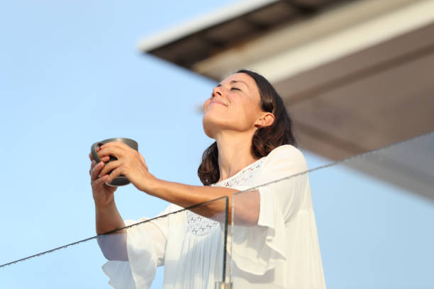 donna adulta con tazza di caffè che respira su un balcone - balcony foto e immagini stock