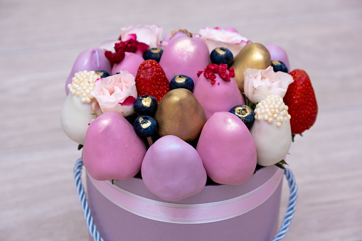 The most beautiful bouquet of fresh strawberries in white, pink and gold chocolate on a light background