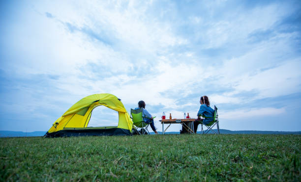 友人を持つアジアの女性観光客は夕日に湖の近くでキャンプをしながら、夏に幸せと一緒にビールを飲みます - camping family nature tent ストックフォトと画像