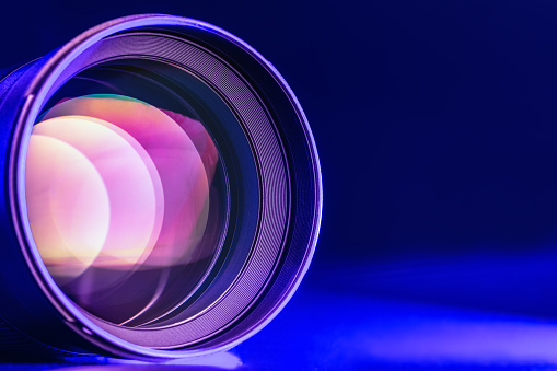 The camera lens with blue light. Close-up of the camera lens on a black background blue illumination. Optics.
