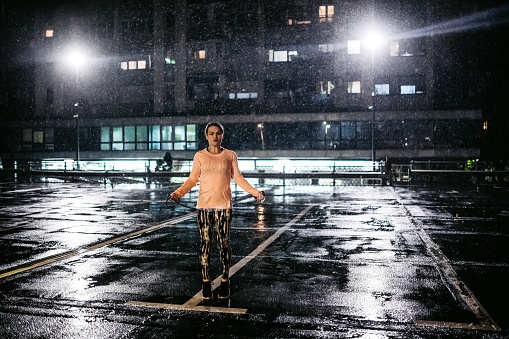 Fit athlete woman skipping rope in the rain on parking garage