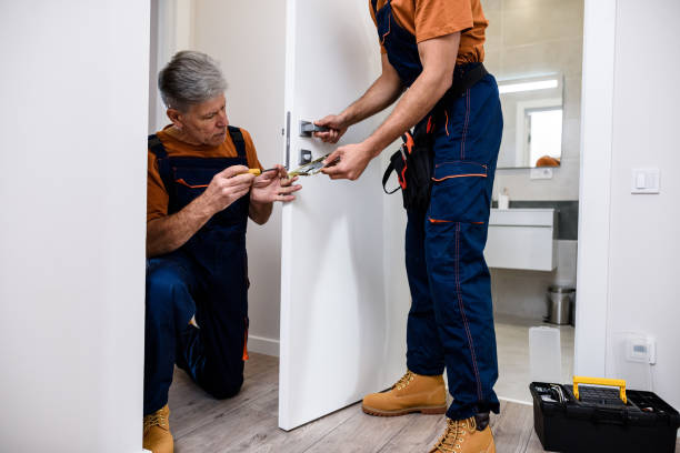 istock Aged locksmith, repairman, worker in uniform installing, working with house door lock using screwdriver while his colleague bringing him lock plate. Repair, door lock service concept 1257902376