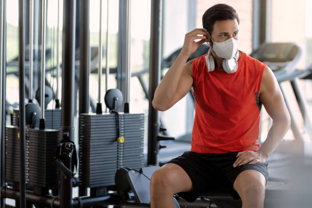 istock Athletic man preparing for workout and putting on protective face mask in a gym. 1257906293