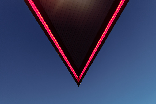 The roof of the gas station with red lighting against the blue evening sky. In the frame, the roof edge is in the shape of a triangle. High quality photo