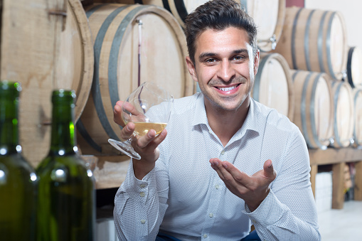 positive adult man having glass with brandy in winery store