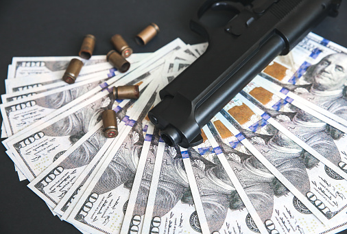 Gun with bullets lying on the table. Money on black background. Criminal problems. Dollars.