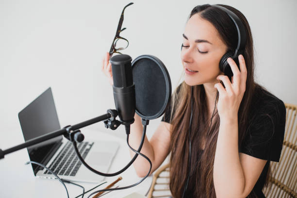 매력적인 젊은 여성 블로거 는 그녀의 노트북, 헤드폰 및 전문 마이크를 사용하여 온라인 팟 캐스트를 녹음. - microphone mid air recording studio radio station 뉴스 사진 이미지