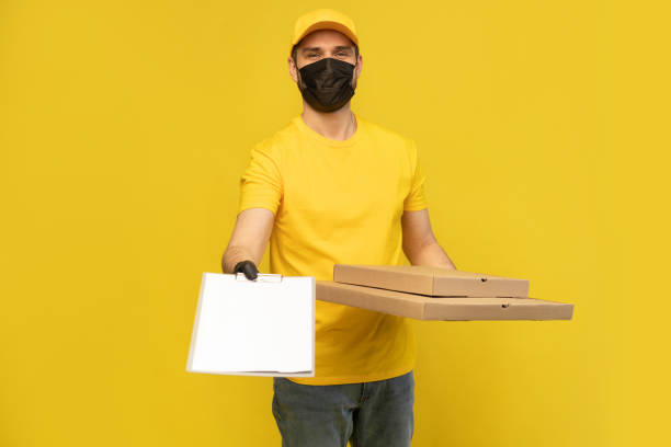istock Pizza delivery man in mask looking at camera isolated on yellow background. Coronavirus 2019-ncov concept. 1257915739