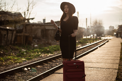 Young woman wearing black dress waiting for a train at the railroad station on a lovely sunny day