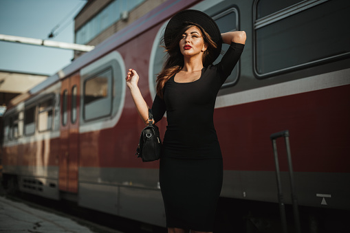 Portrait of a beautiful young woman holding a hat on a windy day at the railroad station