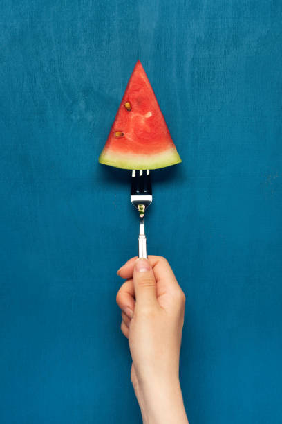 Hand holds work with watermelon slice on blue wooden background. Flat lay. Top view.